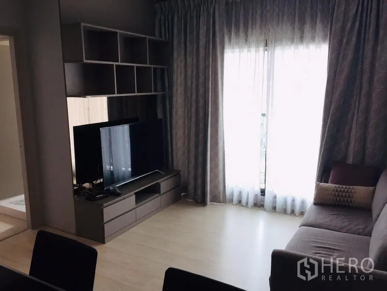 คอนโด ให้เช่าในKhlong Toei, Bangkok - ห้องนั่งเล่นมีโซฟา ชุดชั้นวางทีวี และประตูกระจกสูงจรดเพดานออกสู่ระเบียงพร้อมผ้าม่าน