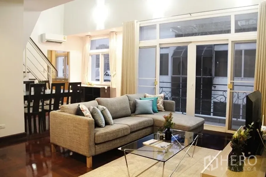 Apartment for rent in Khlong Toei, Bangkok - Open-plan lounge with L-shaped sofa, glass coffee table and balcony doors