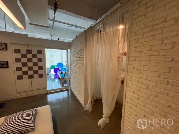 พื้นที่ขายปลีก ให้เช่า - พื้นที่ภายในสว่าง ผนังอิฐสีขาว ผ้าม่านโปร่ง และพื้นคอนกรีตมันวาว มองไปยังสตูดิโอที่มีลูกบอลออกกำลังกาย