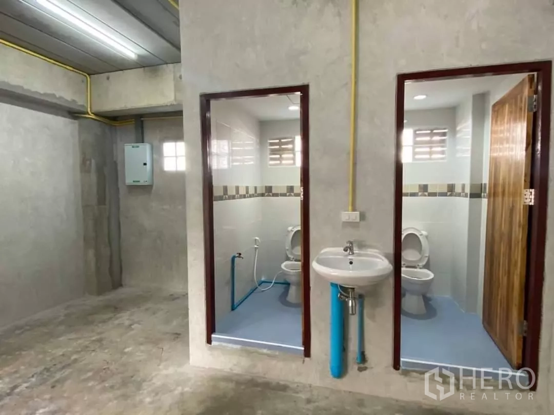 Warehouse for rent in Min Buri, Bangkok - Clean restroom area with two toilet cubicles and a wall-mounted sink inside the warehouse.