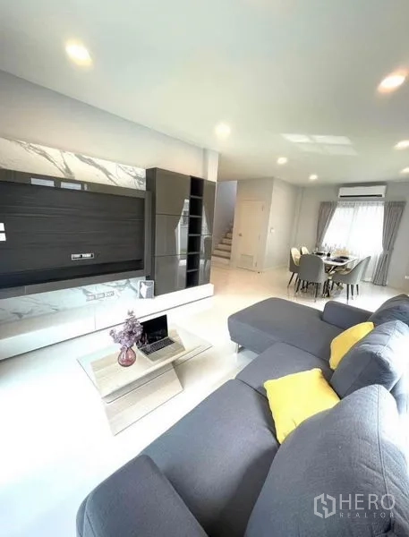 Detached House for rent - Open-plan lounge with TV feature wall, gray sofa and view toward the dining zone.