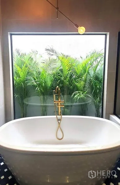 Home Office for rent or sale in Khlong Toei, Bangkok - Bathroom featuring a freestanding tub, brass fixtures and a large window to lush green plants.