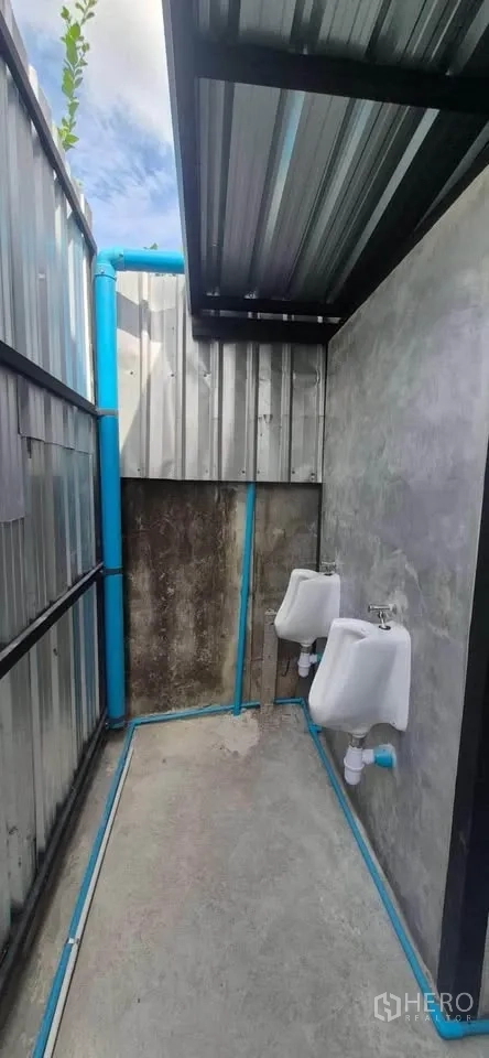 Warehouse for rent in Lat Phrao, Bangkok - Outdoor urinal area with roof cover, visible water pipes, and concrete floor.