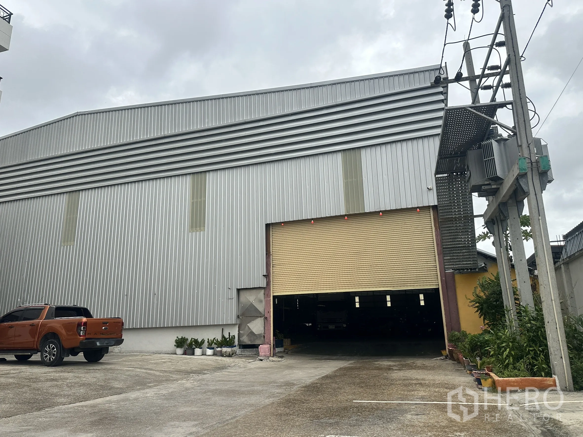 Warehouse for rent in Mueang Samut Prakan, Samut Prakan - Front facade of the warehouse showing loading area and parking beside the entrance.