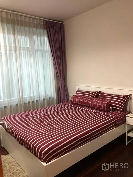Condominium for sale in Ratchathewi, Bangkok - Cozy bedroom with red striped bedding on a white bed and a large window with sheer curtains.