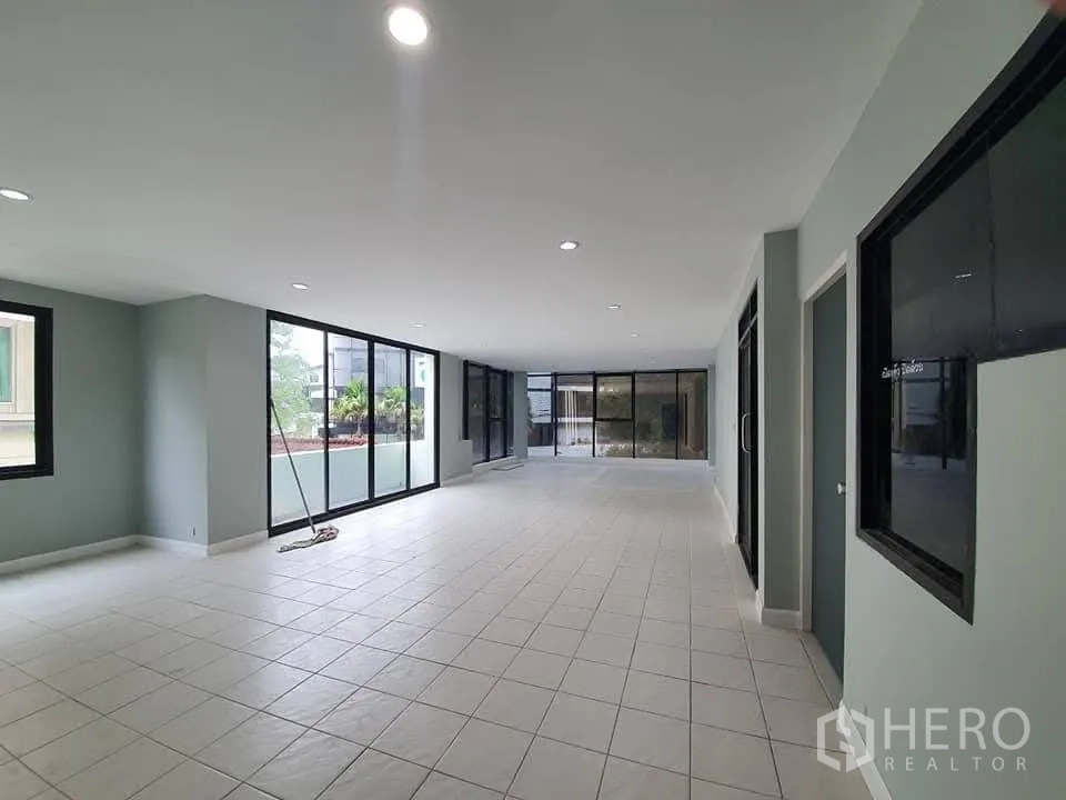 Home Office for rent in Wang Thonglang, Bangkok - Open‑plan floor with white tiles and full‑height glass walls overlooking a terrace.