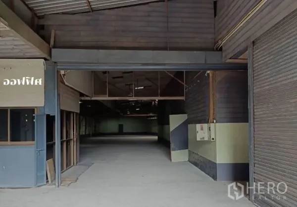 货栈 出租在Bang Khen, Bangkok - 曼谷邦肯仓库入口，卷帘门、办公室小隔间与宽阔混凝土地面。