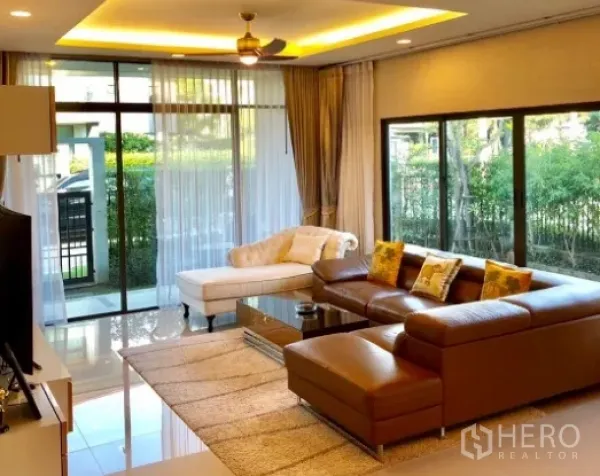 Detached House for rent in Bang Kapi, Bangkok - Bright living room with floor-to-ceiling windows, L-shaped leather sofa, chaise lounge and garden views.
