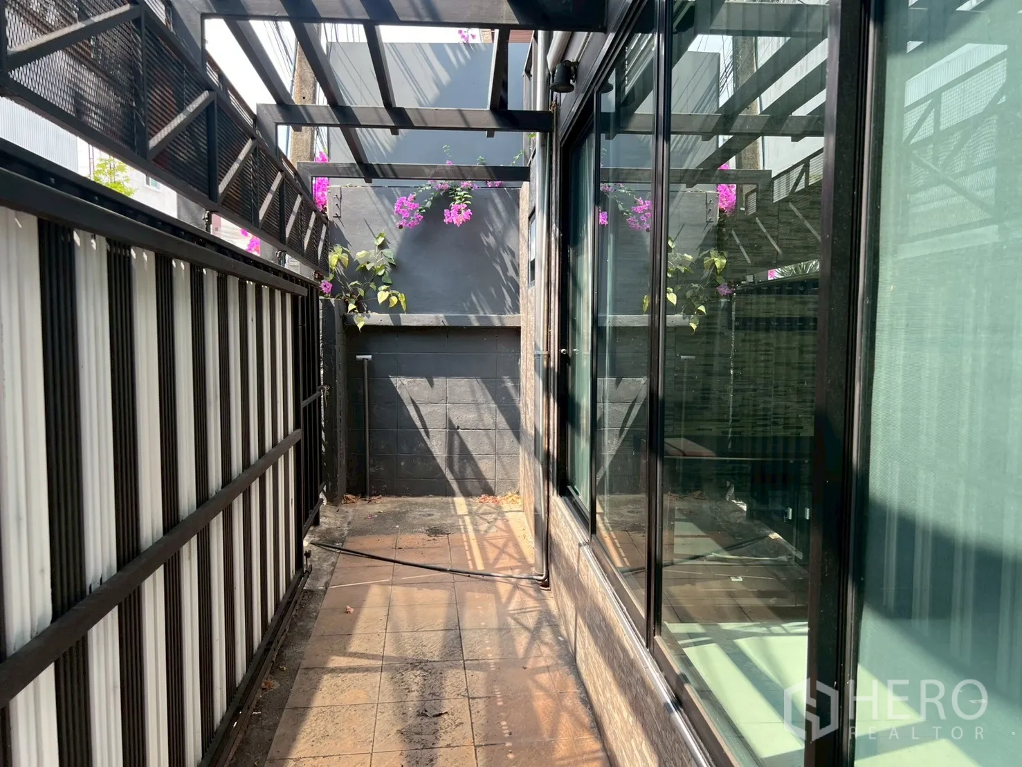 Detached House for rent or sale in Wang Thonglang, Bangkok - Narrow side terrace with glass wall, tiled floor and metal canopy with flowers.