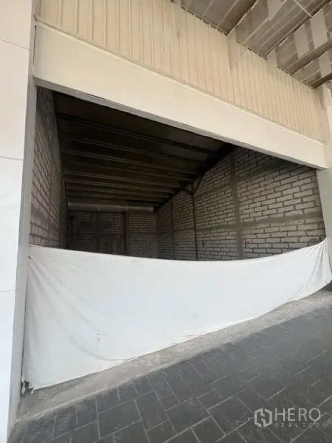 พื้นที่ขายปลีก ให้เช่าในKhlong Toei, Bangkok - ด้านหน้าอาคารกว้าง ใต้กันสาด มีผ้าใบกั้นและลานคอนกรีต หน้าพื้นที่ยังไม่ตกแต่ง