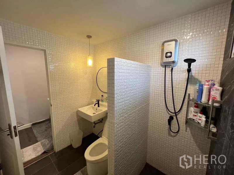 独立式住宅 出售在Bang Kruai, Nonthaburi - 卫生间铺白色马赛克，淋浴区配即热式热水器，含洗手盆与坐便器。