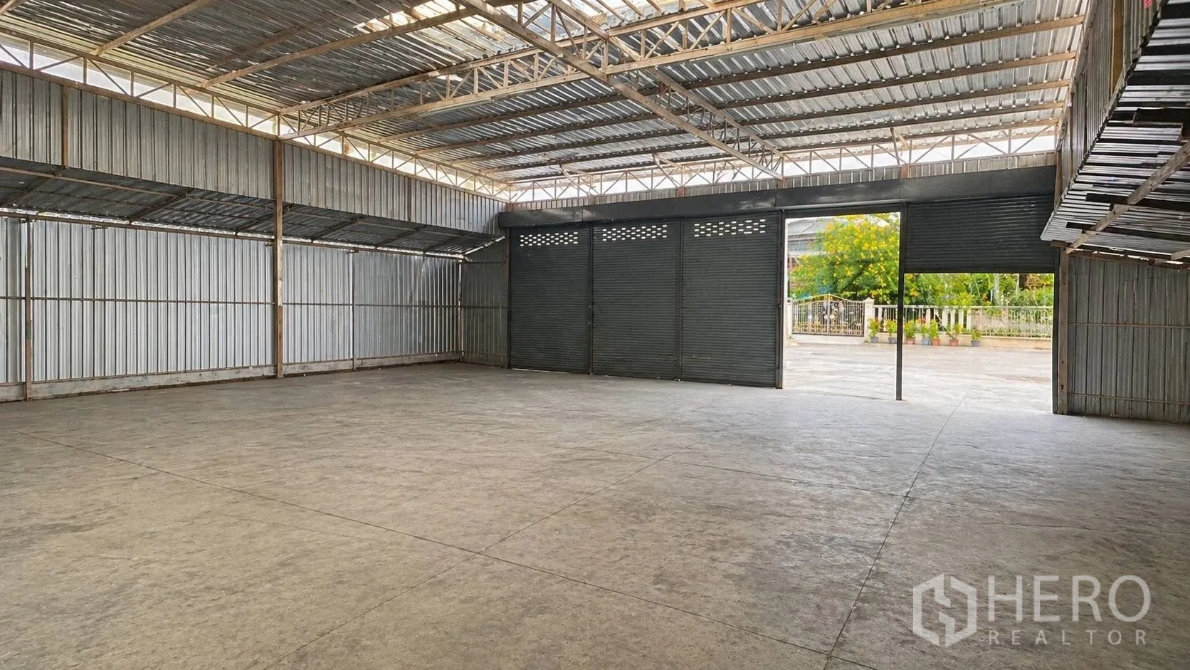 โกดัง for rent in Don Mueang, Bangkok - ภายในโกดังแบบเปิดโล่ง มีโครงหลังคาเหล็ก พื้นคอนกรีต และประตูม้วนขนาดใหญ่เชื่อมสู่ลานด้านหน้า