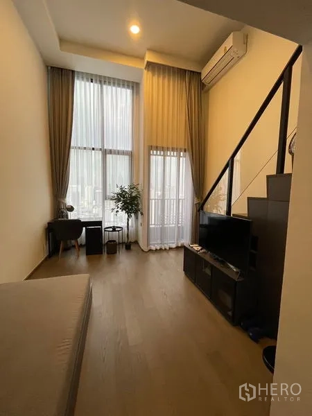 公寓 出租在Bang Rak, Bangkok - 挑高客厅，落地窗、窗帘、电视柜与书桌，采光充足的阁楼风格。