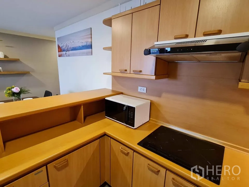 Condominium for rent in Khlong Toei, Bangkok - Close-up of kitchen with induction cooktop, range hood and microwave.