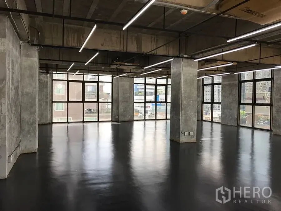 Office Space for rent in Khlong Toei, Bangkok - Open-plan industrial office with polished floors, exposed concrete columns, LED strip lighting and large windows.