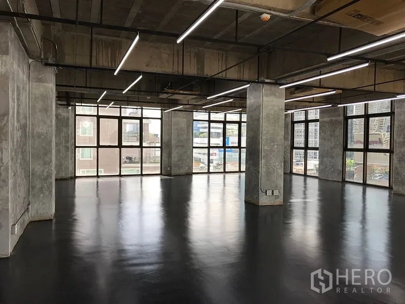 Office Space for rent in Khlong Toei, Bangkok - Open-plan industrial office with polished floors, exposed concrete columns, LED strip lighting and large windows.