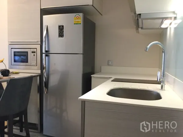 公寓 出租或出售在Watthana, Bangkok - 紧凑厨房，配不锈钢双门冰箱、嵌入式微波炉、水槽与电磁炉。