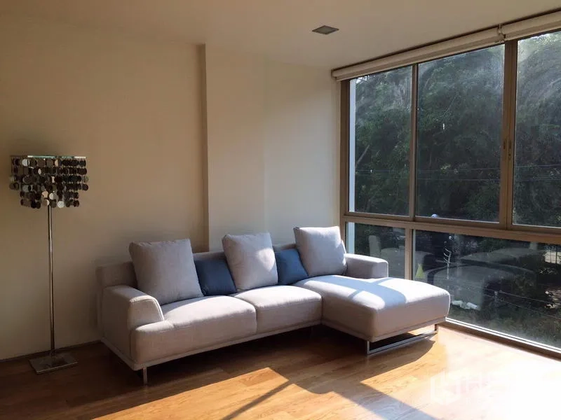 คอนโด ให้เช่าในKhlong Toei, Bangkok - ห้องนั่งเล่นสว่าง โซฟาเข้ามุมสีอ่อน โคมตั้ง และหน้าต่างบานใหญ่เห็นวิวต้นไม้