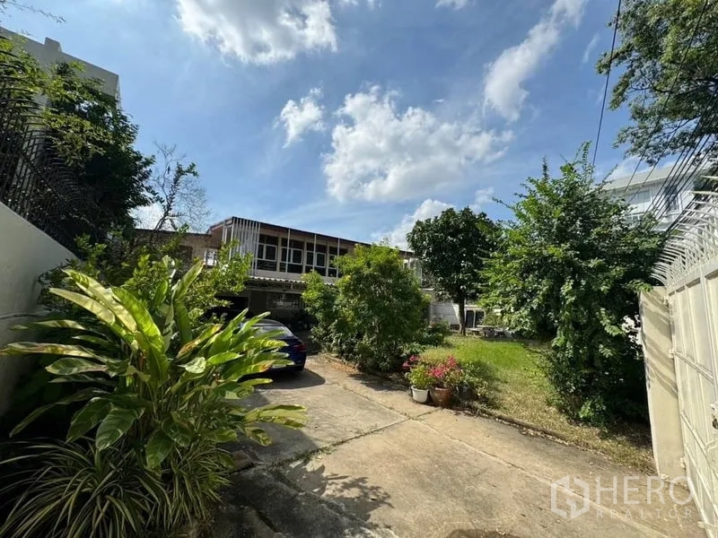 独立式住宅 出租在Watthana, Bangkok - 宽敞前院与车道，绿树成荫，通往一栋独立屋，蓝天晴朗。