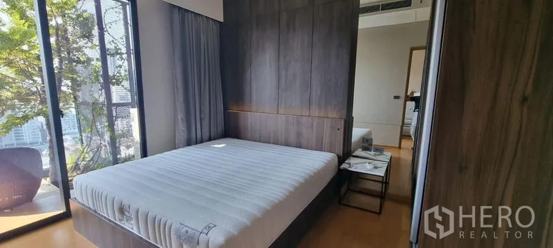 คอนโด ขายในWatthana, Bangkok - ห้องนอนสว่างด้วยกระจกเต็มบาน ตู้เสื้อผ้าไม้ และทางออกสู่ระเบียงพร้อมต้นไม้และวิวเมือง