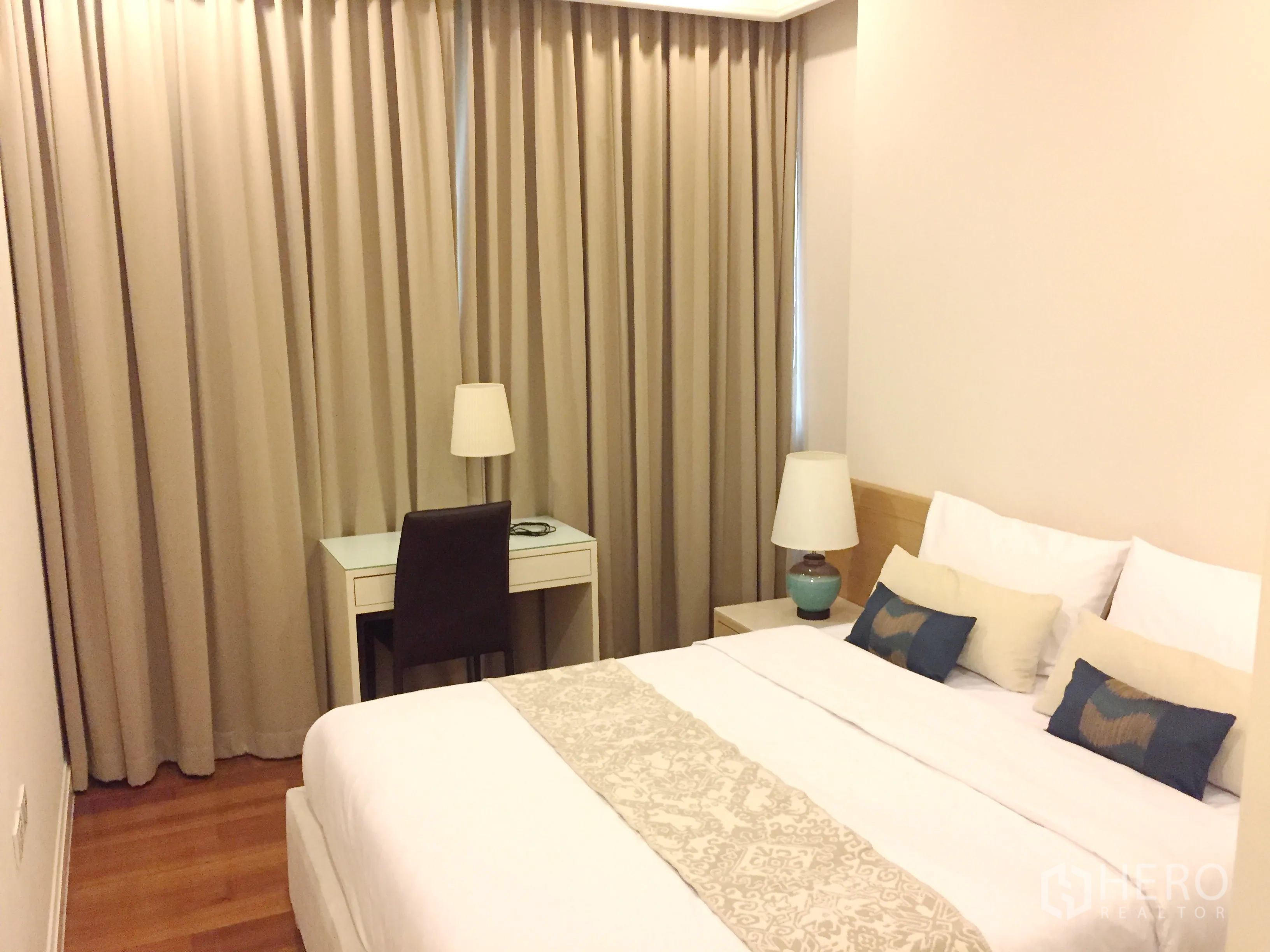 Condominium for rent in Pathum Wan, Bangkok - Cozy bedroom with king bed, work desk, lamps and floor-to-ceiling curtains.