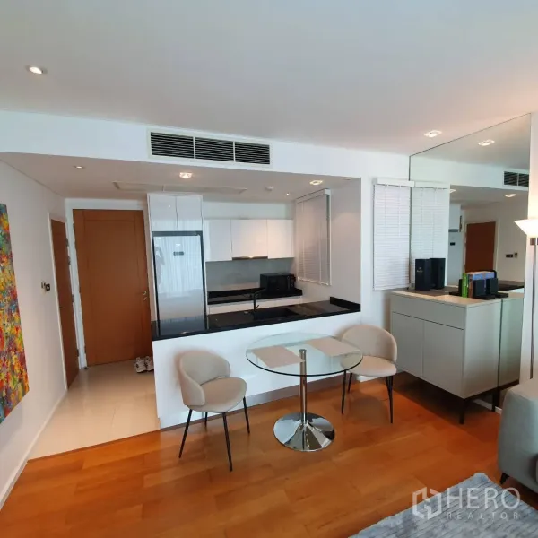 Condominium for rent in Watthana, Bangkok - Modern kitchenette with black countertop, built-in hob and seating for two in the living area.
