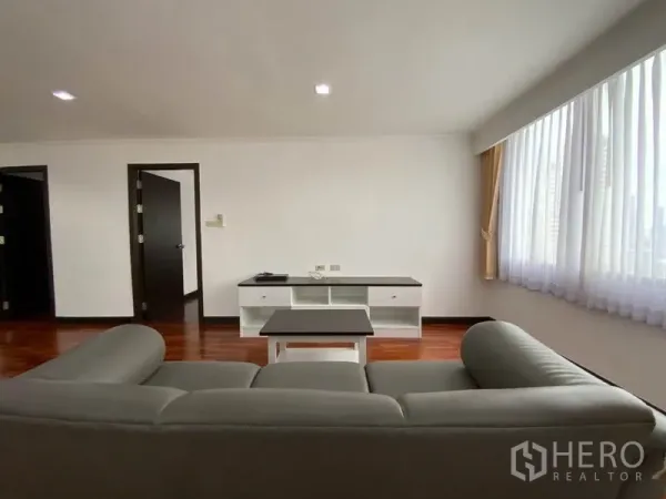 คอนโด ให้เช่าในWatthana, Bangkok - ห้องนั่งเล่นมินิมอล โซฟาสีเทา ชั้นวางทีวี และหน้าต่างบานกว้างรับแสงธรรมชาติบนพื้นไม้ขัดเงา