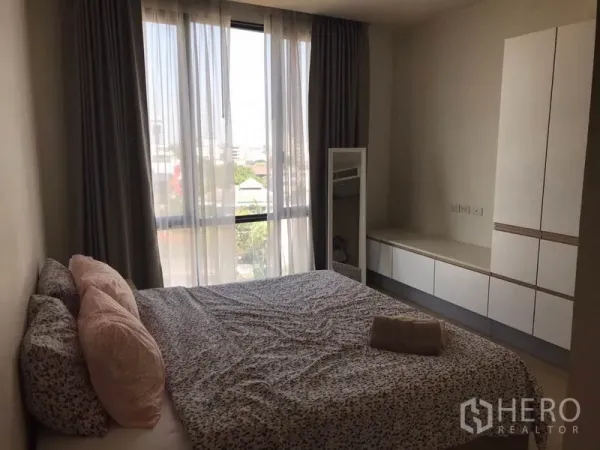 Condominium for rent in Watthana, Bangkok - Cozy bedroom with large window, sheer curtains and built-in wardrobes in a modern condominium.
