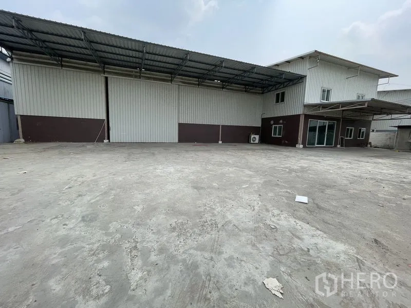 Warehouse for rent in Lat Lum Kaeo, Pathum Thani - Wide concrete loading area before a steel warehouse with attached two-storey office and canopy.