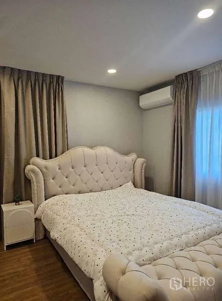 Detached House for rent in Bang Phli, Samut Prakan - Master bedroom with tufted headboard bed, bedside table and warm-toned curtains.