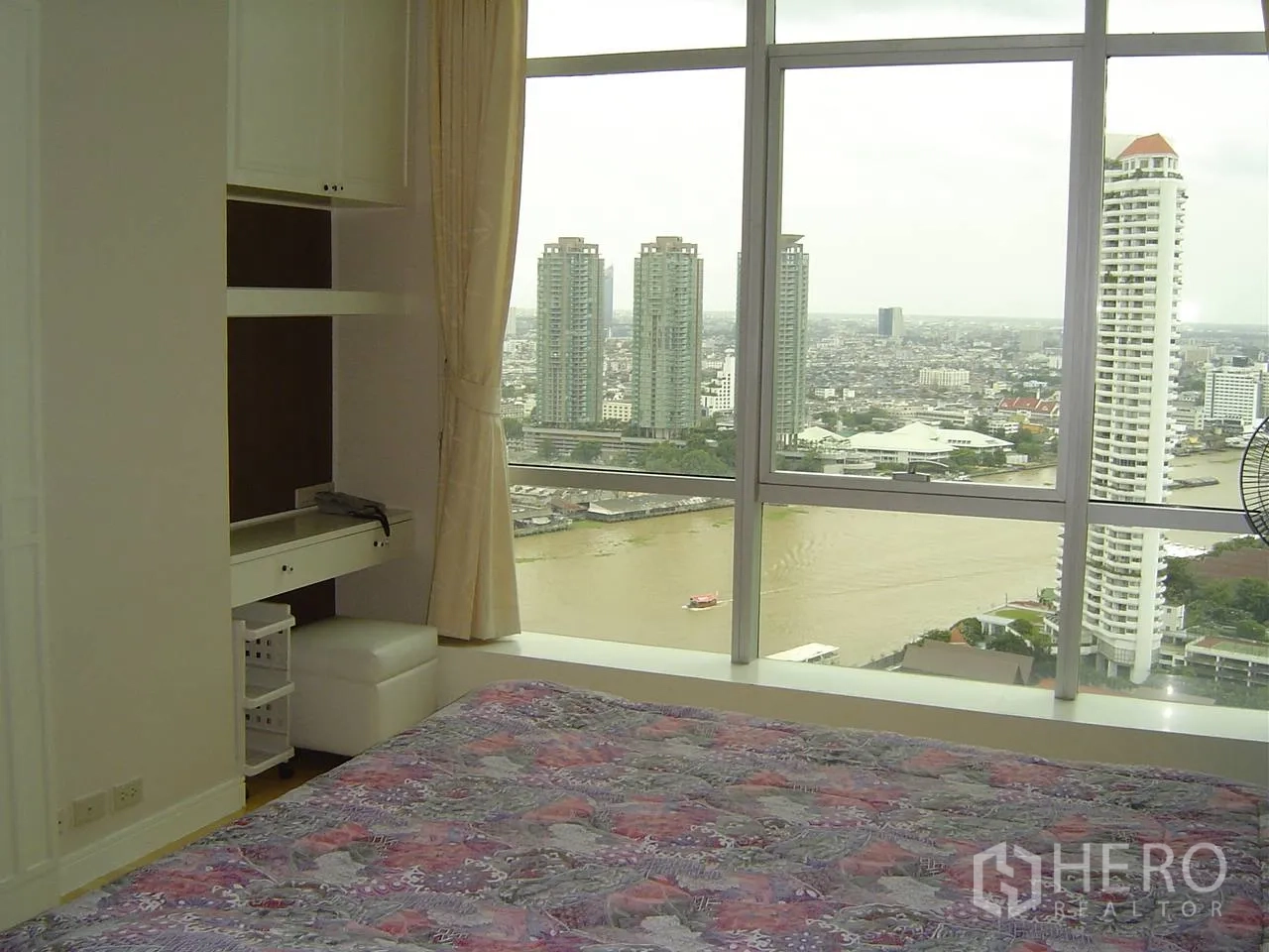 公寓 出租在Khlong San, Bangkok - 卧室设落地窗与窗帘，带内置书桌，俯瞰湄南河及曼谷天际线。