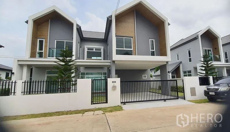 Detached House for sale in Lam Luk Ka, Pathum Thani - Modern detached house exterior with twin gable roofs, grey facade, wood accents and a gated driveway in Lam Luk Ka.