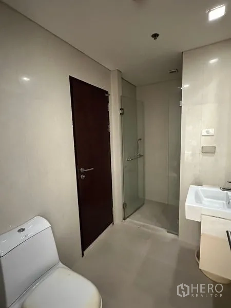 Condominium for sale in Watthana, Bangkok - Modern bathroom with toilet, sink and glass-enclosed shower.