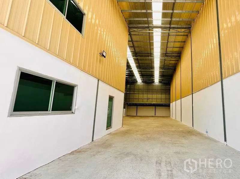 Warehouse for rent in Pak Kret, Nonthaburi - High-clearance warehouse bay with skylights, concrete floor and a side office wall.
