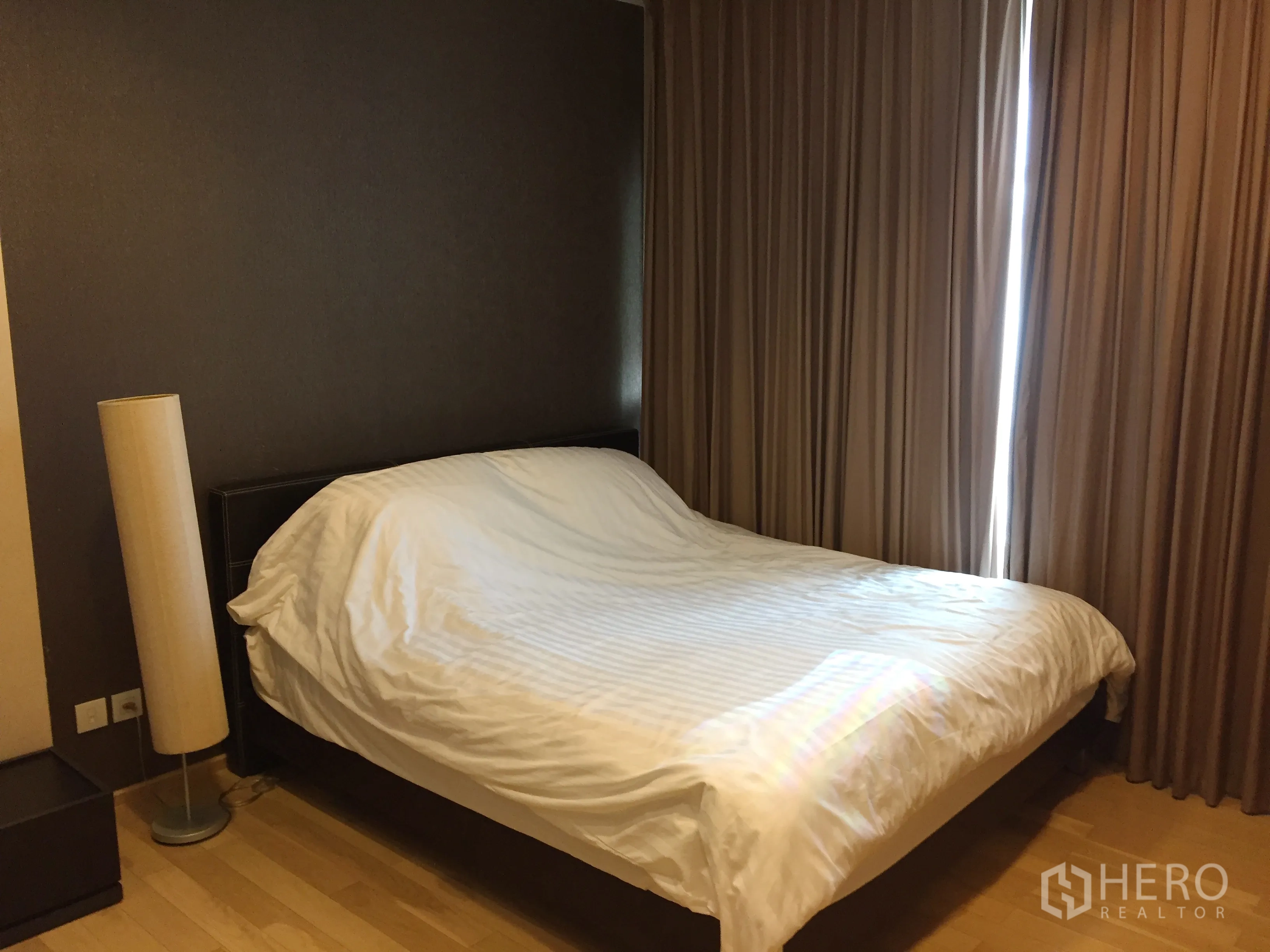 คอนโด ให้เช่าในKhlong Toei, Bangkok - ห้องนอนหลักพร้อมเตียงคู่ พื้นไม้ โคมไฟยืน และผ้าม่านทึบในคอนโดเขตคลองเตย