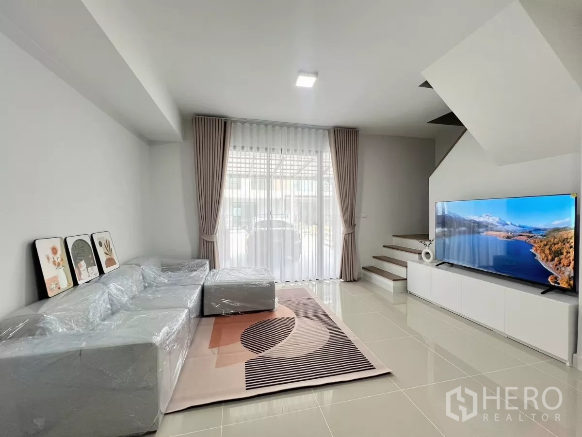 ทาวน์เฮาส์ ให้เช่าในBang Phli, Samut Prakan - ห้องนั่งเล่นสว่าง โซฟาขนาดใหญ่ ตู้ทีวี และบันไดขึ้นชั้นบน