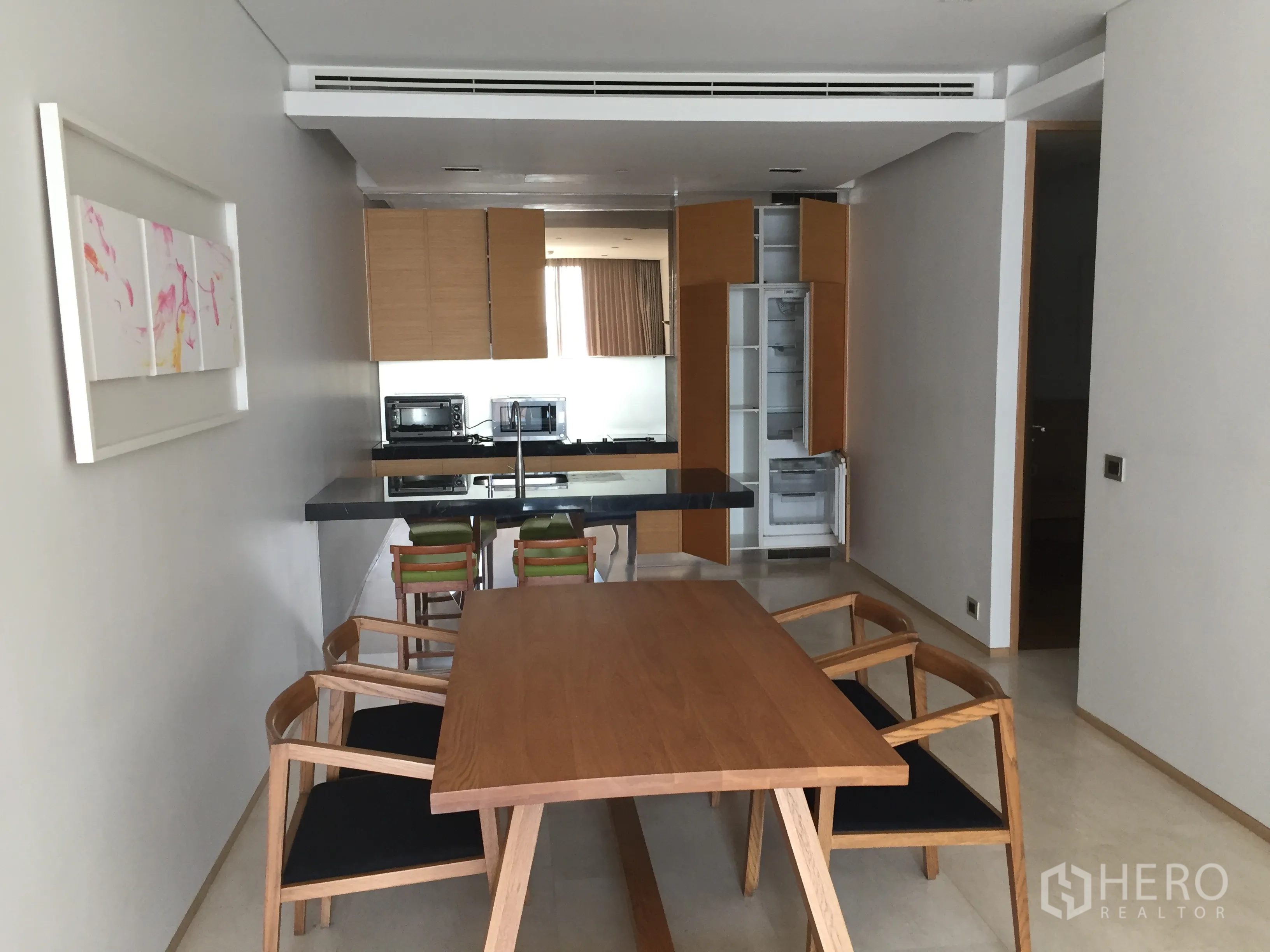 公寓 出租在Bang Rak, Bangkok - 餐区木质餐桌椅，面对开放式厨房，设岛台与嵌入式家电。