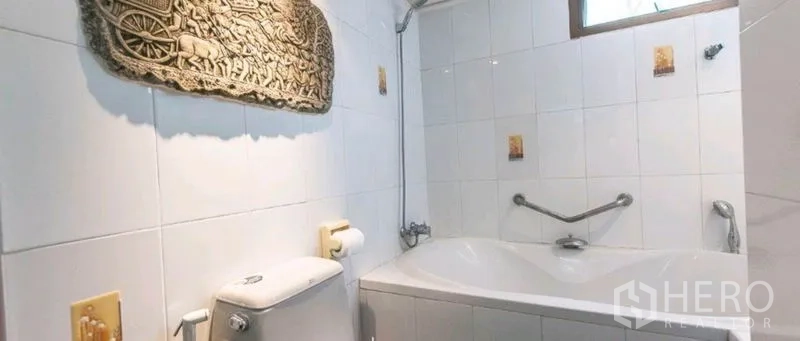 Condominium for rent in Watthana, Bangkok - Bathroom with white tiles and a bathtub with safety handrails.