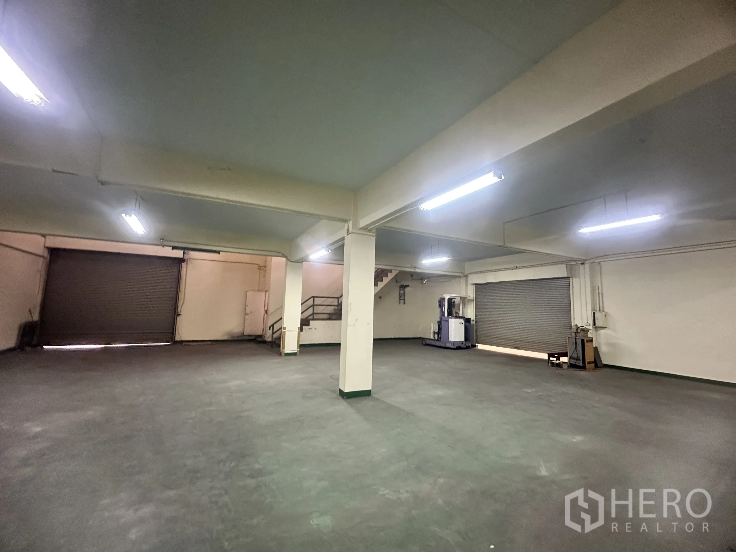 Factory for sale in Bang Bua Thong, Nonthaburi - Ground-floor storage area with multiple roller shutters and equipment.