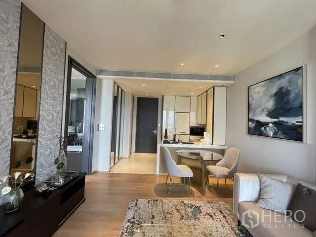 Condominium for rent or sale in Khlong Toei, Bangkok - Living room with mirrored media console facing a compact kitchen and sliding door to the bedroom.