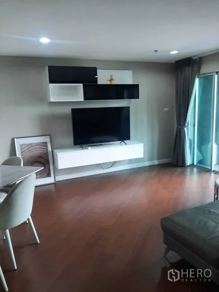 Condominium for rent or sale in Huai Khwang, Bangkok - Bright living room with wall-mounted TV, floating shelves and sliding glass doors to the balcony