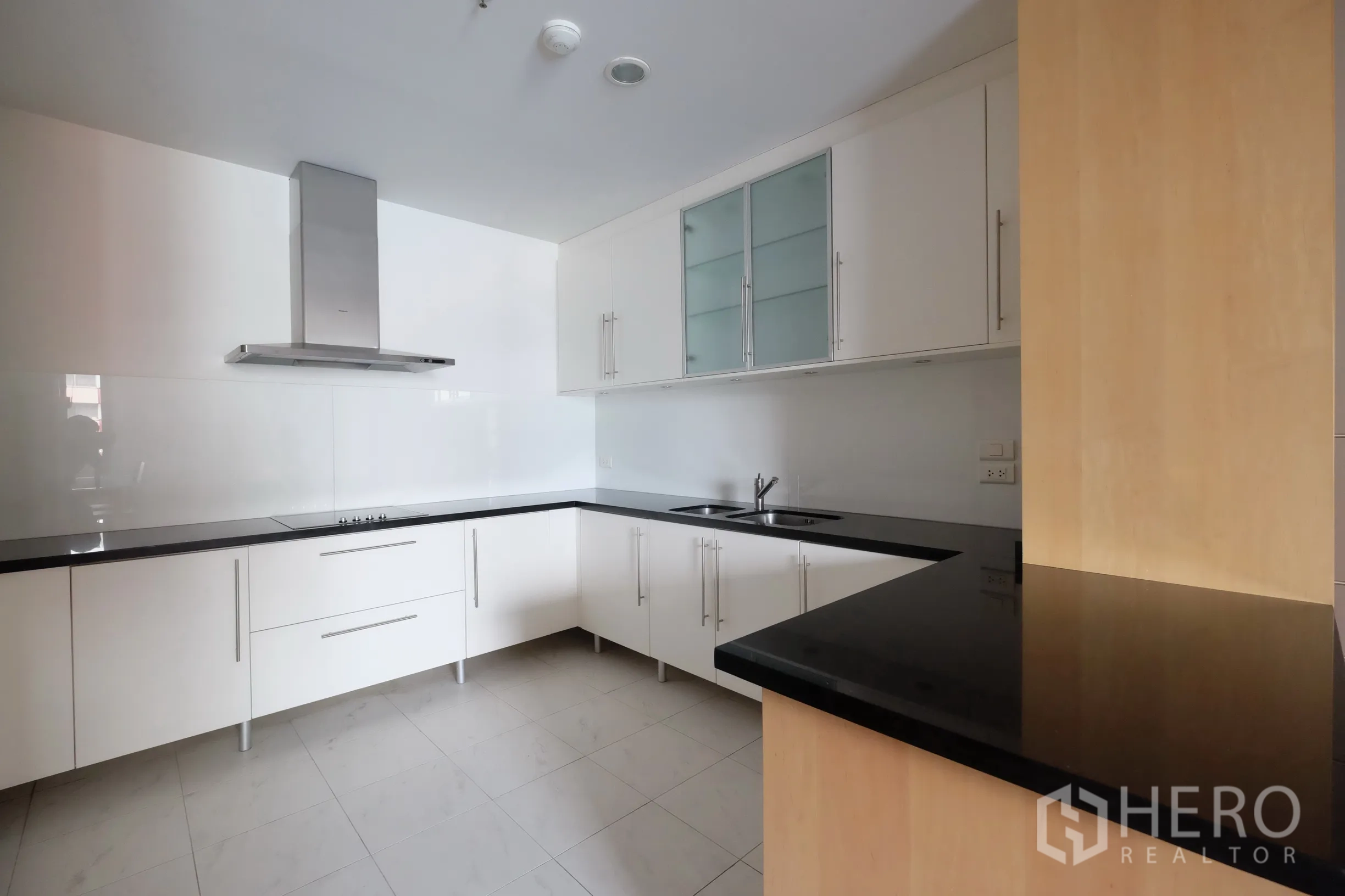 公寓 出租在Bang Rak, Bangkok - L形厨房布局，抽油烟机、双水槽与磨砂玻璃吊柜。