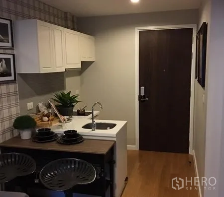 公寓 出租在Khlong Toei, Bangkok - 入口小厨房，白色橱柜、带水槽的岛台与木地板的曼谷公寓。