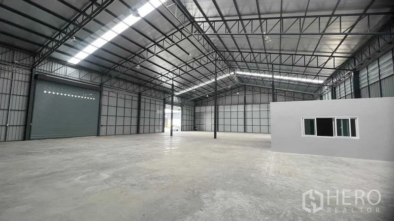 Warehouse for rent in Pathum Thani - Spacious clear-span warehouse interior with high steel truss roof, polished concrete floor, large roller shutter and internal office windows.