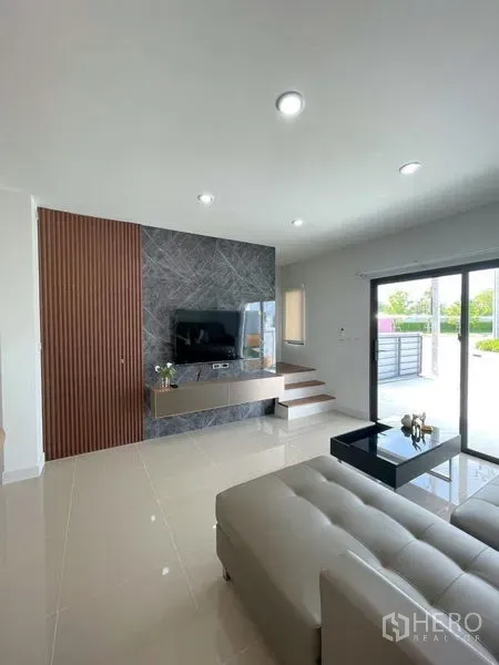 Townhouse for rent in Bang Phli, Samut Prakan - TV feature wall with marble accents facing a modern living area and steps to the entry, opening to a front patio.