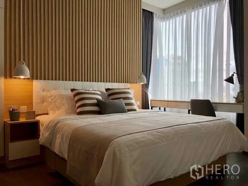 Condominium for rent in Watthana, Bangkok - Corner bedroom with large bed, striped cushions, pendant lights, desk and sheer drapes revealing skyline.