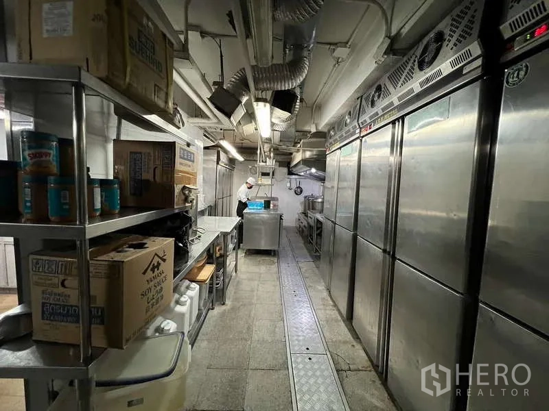 店屋 出租或出售在Khlong Toei, Bangkok - 长形商业厨房，带排烟罩、冰箱与不锈钢操作台。