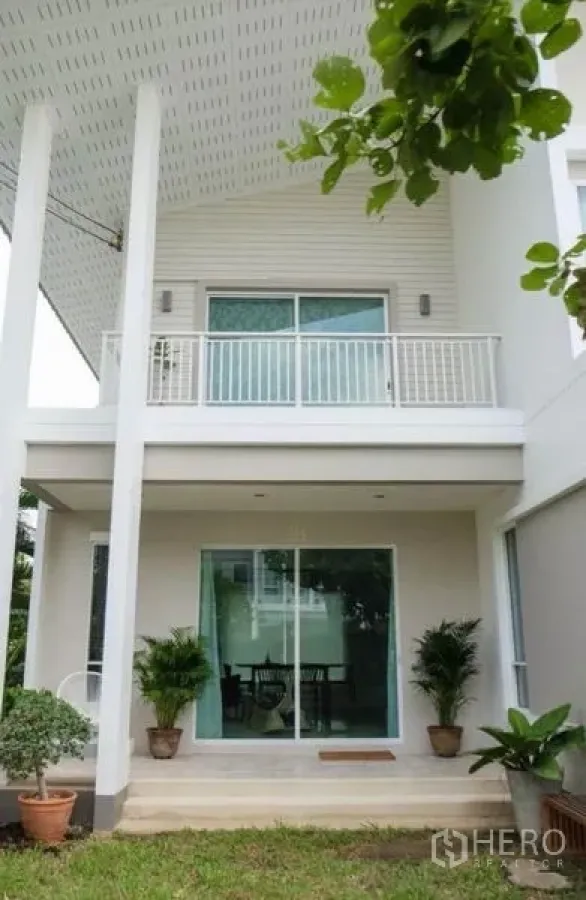 Detached House for rent or sale in Khlong Sam Wa, Bangkok - Modern two-storey white detached house with front patio, sliding glass doors, balcony and potted plants facing the garden.