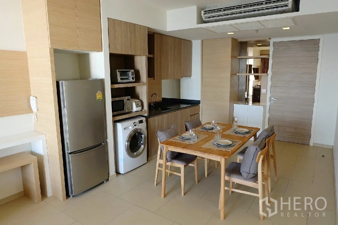 Condominium for rent or sale in Bang Lamung, Chon Buri - Open-plan kitchen and dining area with wood cabinetry, appliances and a washing machine.