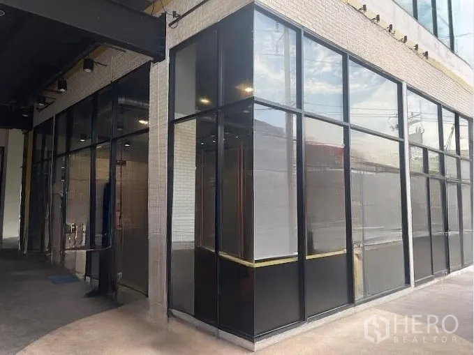 Retail Space for rent - Corner retail unit with floor-to-ceiling glass panels and black metal frames under a covered walkway.